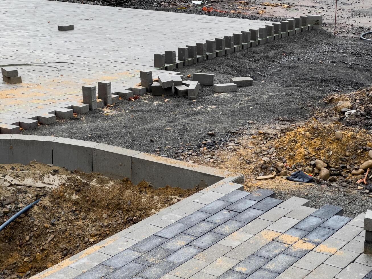 Construction workers are laying paving stones on a new driveway. There are several stones already laid, and others are scattered around photo