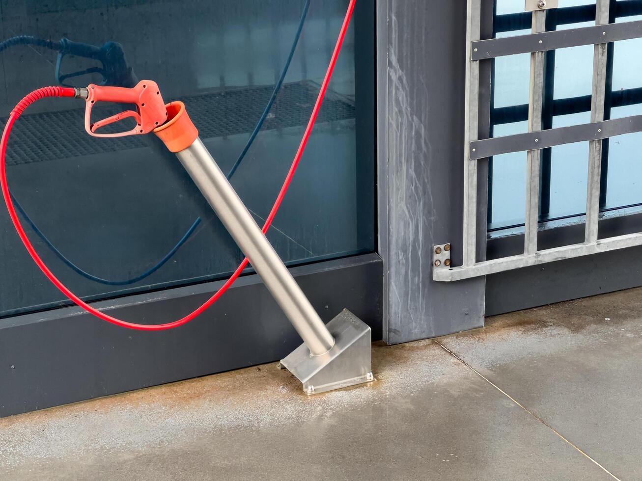 A high-pressure car washer gun stands ready at a car wash, featuring sleek metal design and vibrant red hose, ensuring thorough cleaning of vehicles in progress photo