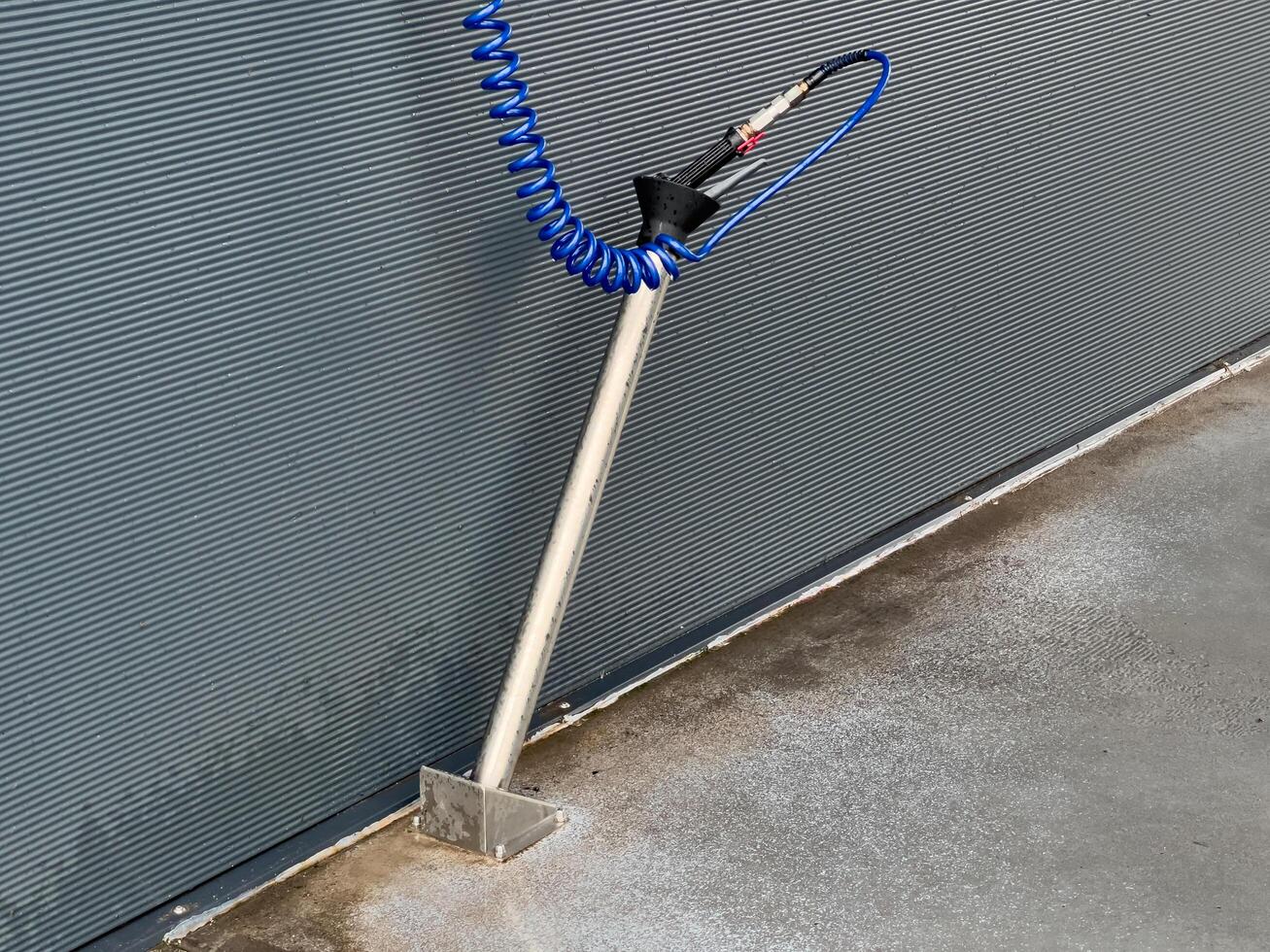 A high-pressure car washer gun stands ready at a car wash location, with a coiled hose extending neatly. This equipment is essential for thorough vehicle cleaning photo
