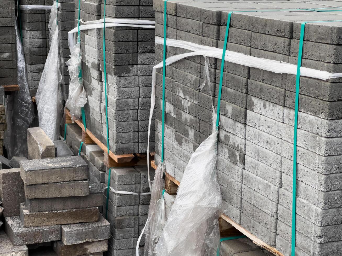 Stacks of gray cobblestone blocks secured with plastic wrap and ropes, prepared for use in a sidewalk construction project in an urban environment photo