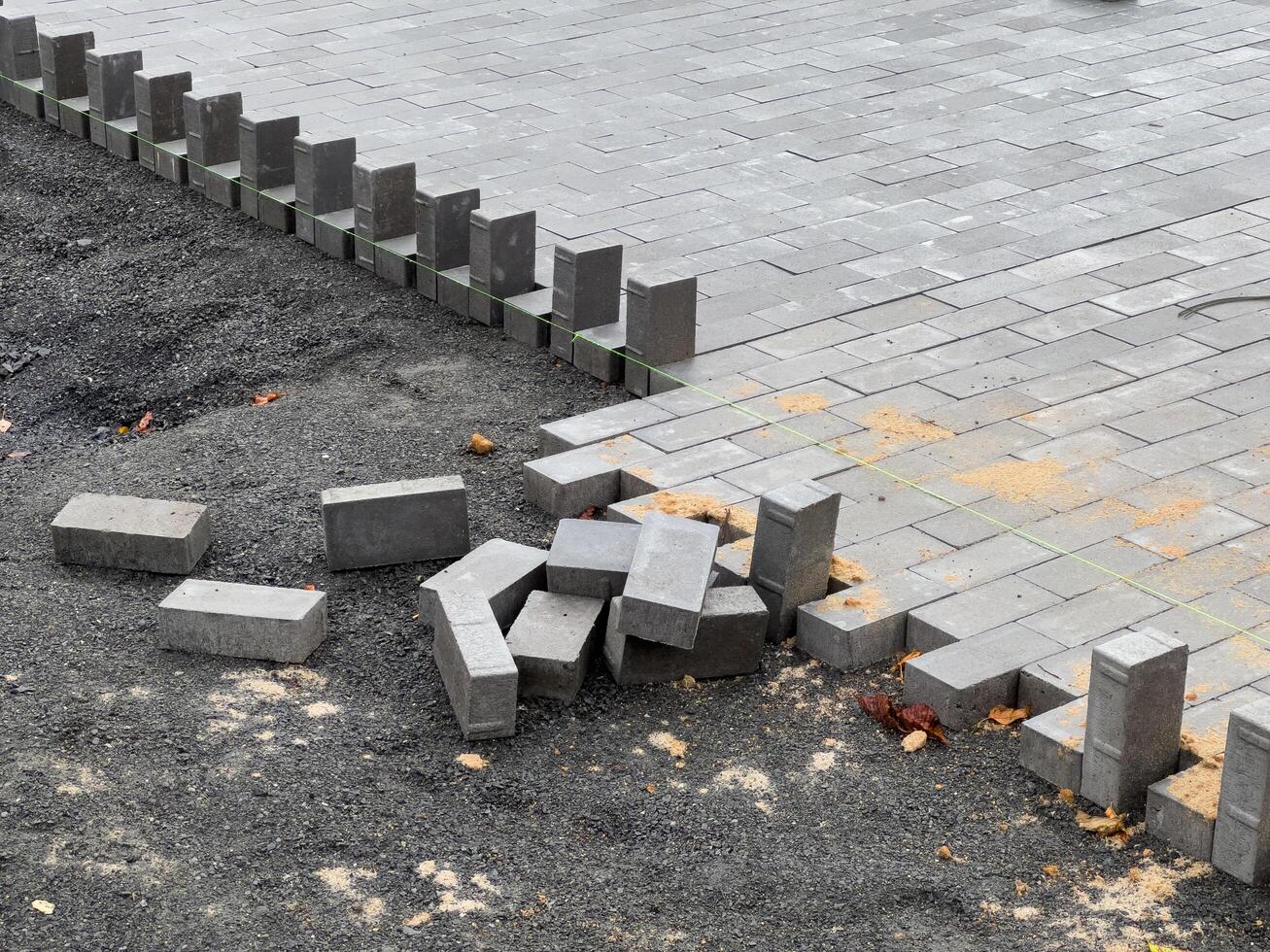 A crew is laying down paving stones to repair a section of pavement. The stones are gray and rectangular, and they are being laid in a pattern. The area around the stones is covered in gravel photo