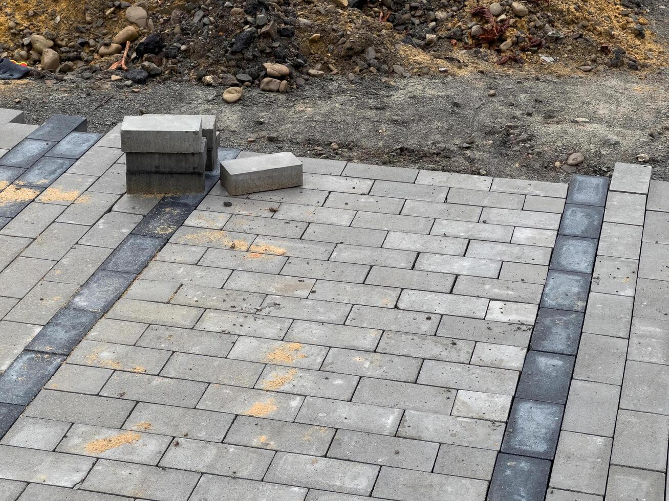 A section of pavement being repaired with gray paving stones. There are a few stones that have been laid in a row, but most of the area is still bare photo