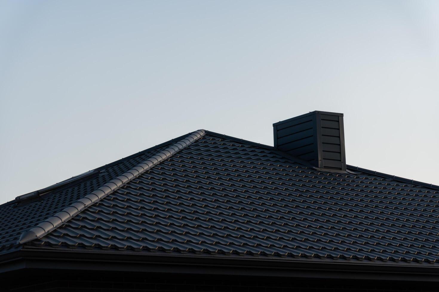 The roof of a modern house features sleek black metal tiles, highlighting contemporary construction techniques and materials under a clear blue sky photo