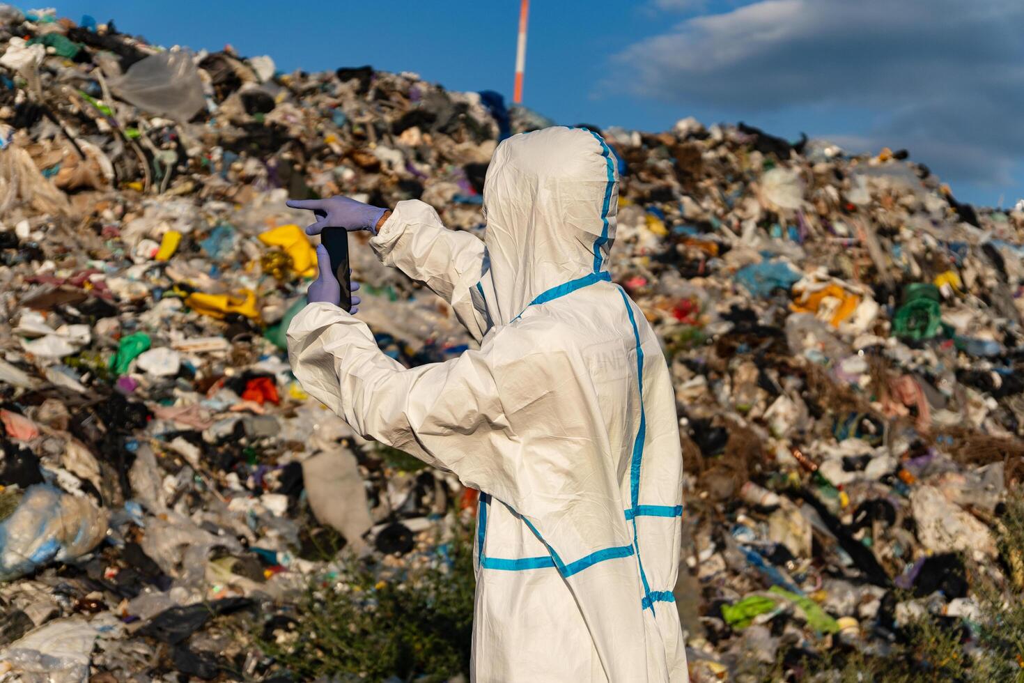Standing in a protective suit, an individual looks out over a vast landfill filled with heaps of waste, evaluating the environmental impact photo