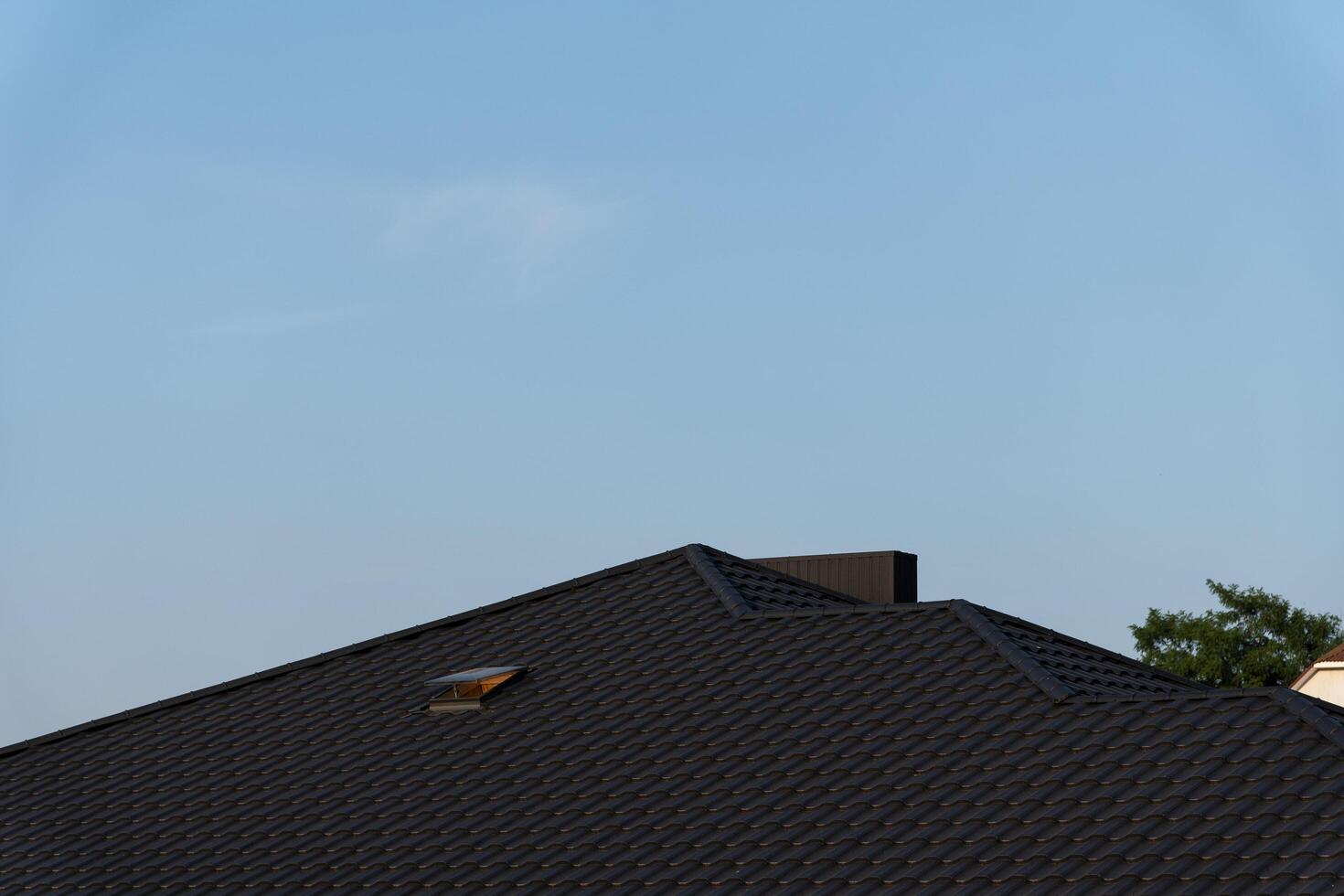A house features a sleek black metal roof that reflects contemporary design trends, contrasting beautifully with the clear blue sky above photo