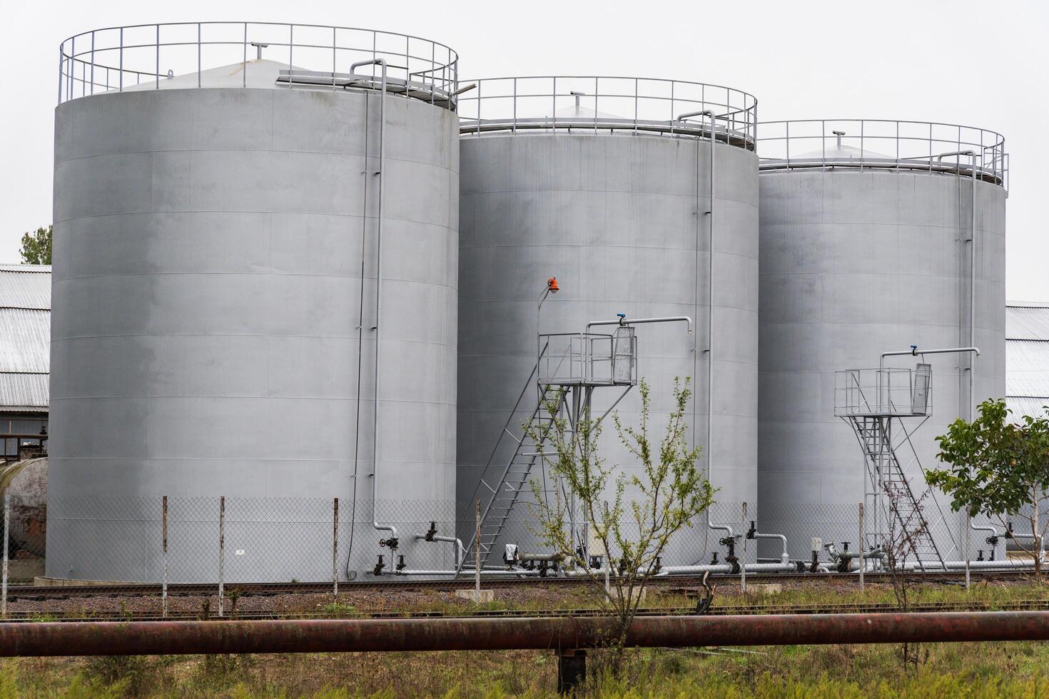 Three large gray storage tanks are positioned closely together at an industrial site. Metal catwalks and ladders provide access for maintenance and monitoring photo