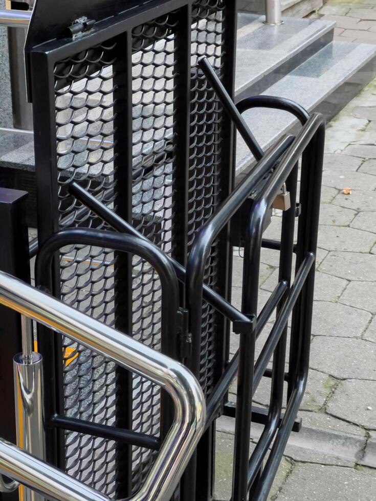 A black metal ramp is folded up, attached to the side of a building. The ramp has a metal mesh surface and a steel handrail. It is likely used to provide access to people with mobility issues photo