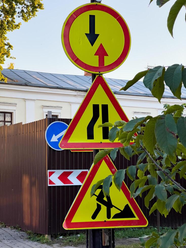 Brightly colored construction signs alert drivers to changing road conditions, including a merge and worker presence, set against a vibrant urban backdrop photo