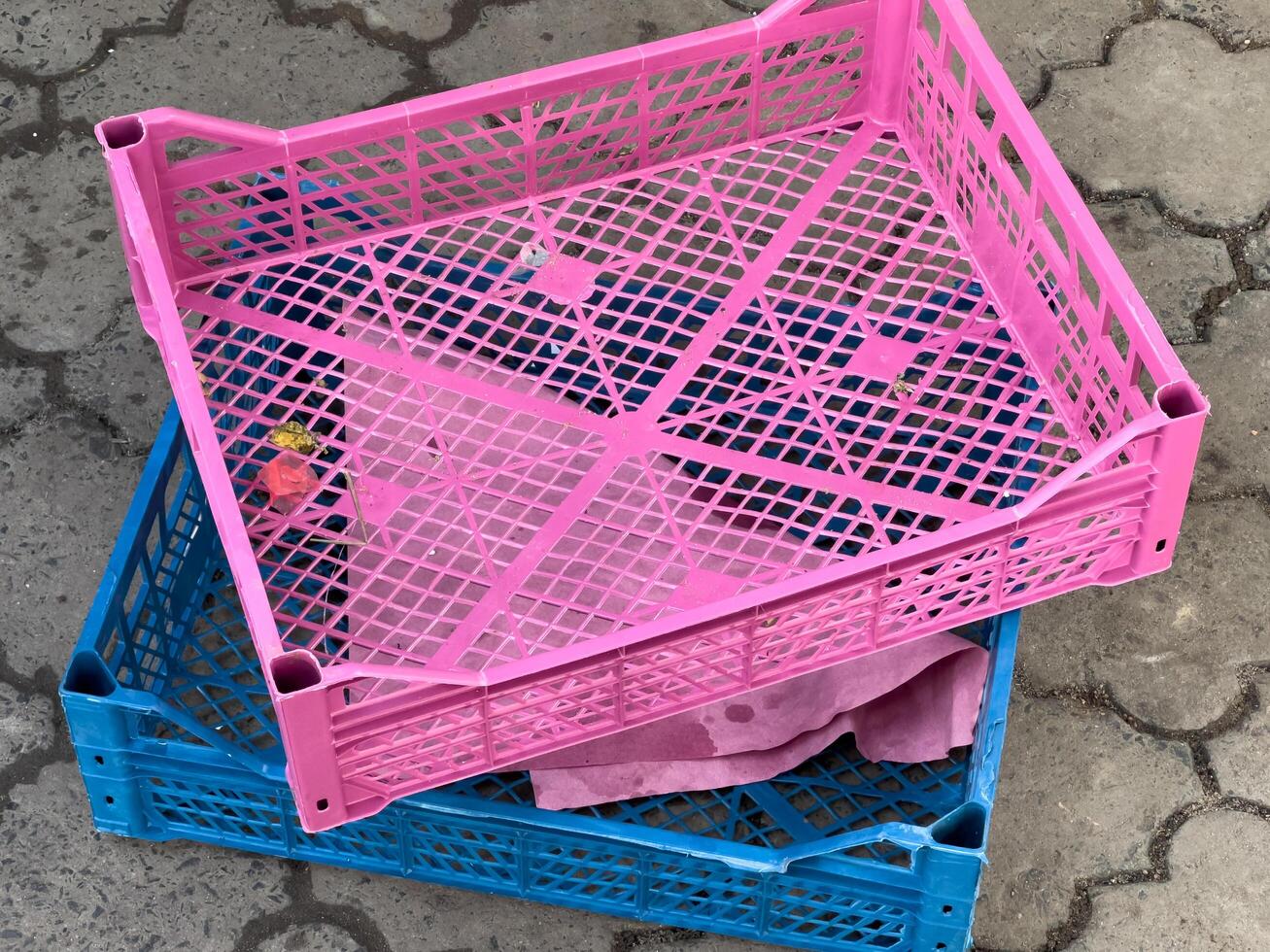 Vibrant pink and blue plastic crates are stacked on a patterned pavement, hinting at their use for storing goods at a lively market atmosphere under the warm sun photo