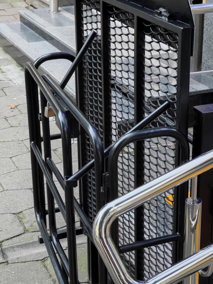 A black metal ramp with a mesh panel folds up against the side of a building, providing wheelchair access photo