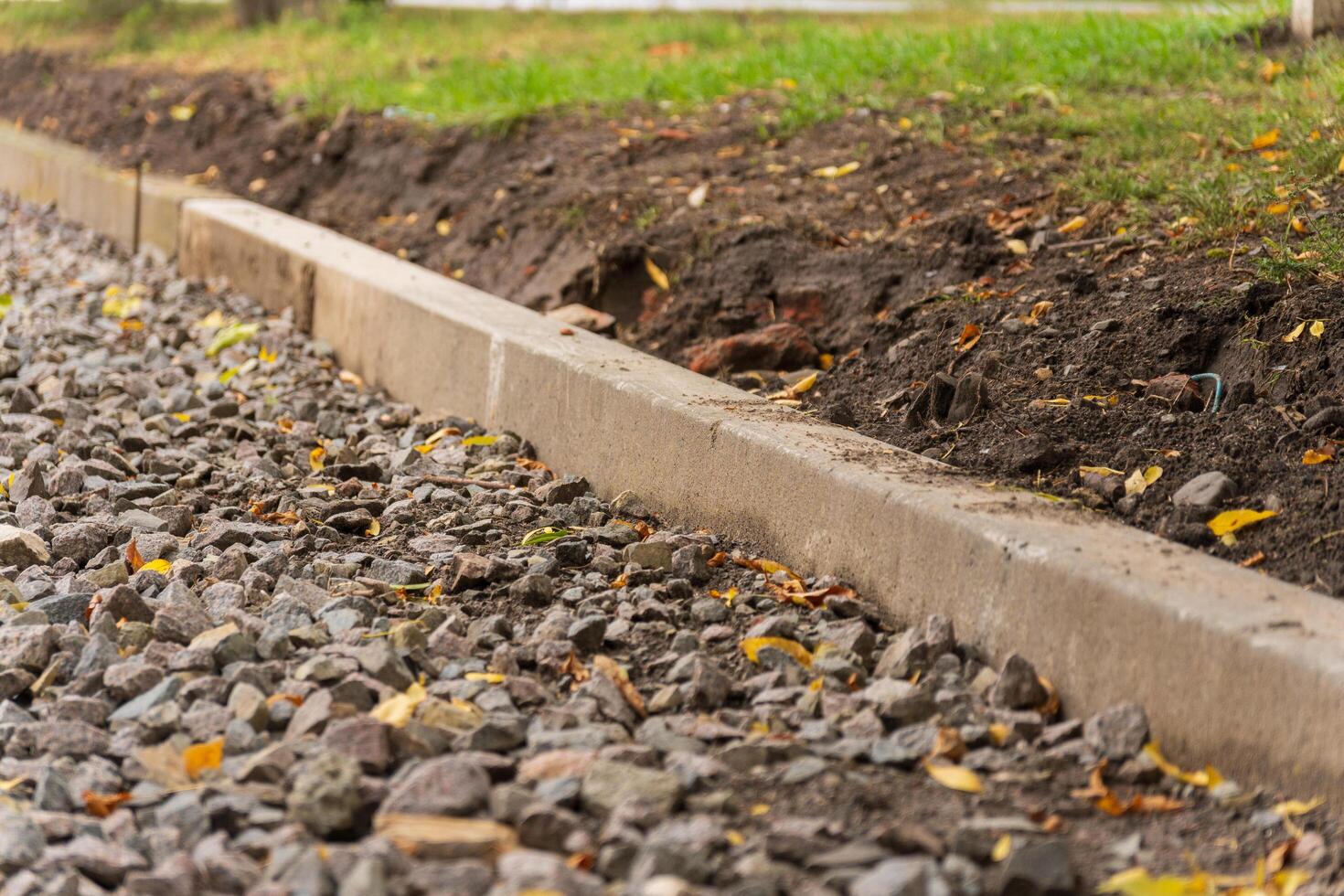 In this tranquil setting, a new gravel path emerges, meticulously edged by a sturdy concrete curb, while vibrant leaves scatter across the ground, inviting exploration photo