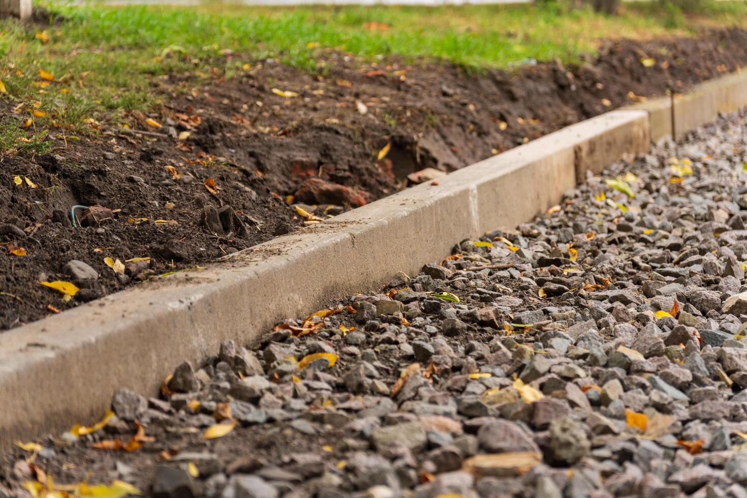 This setting showcases a newly installed concrete curb, contrasting with the scattered gravel and vibrant autumn leaves, capturing the peaceful essence of nature's transition photo