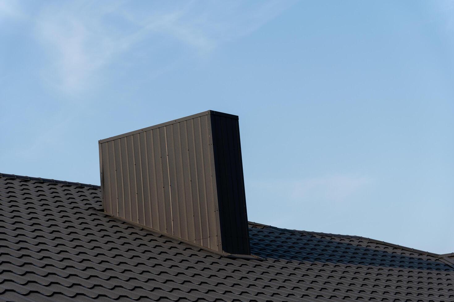 A striking chimney with a unique rectangular shape rises from the rooftop, contrasting against a serene blue sky, illustrating innovative architectural style photo