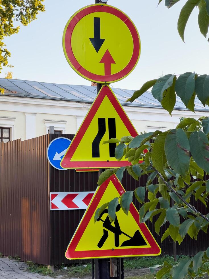 Bright warning signs stand tall in a quiet urban area, guiding vehicles through construction zones and indicating road changes amidst greenery photo
