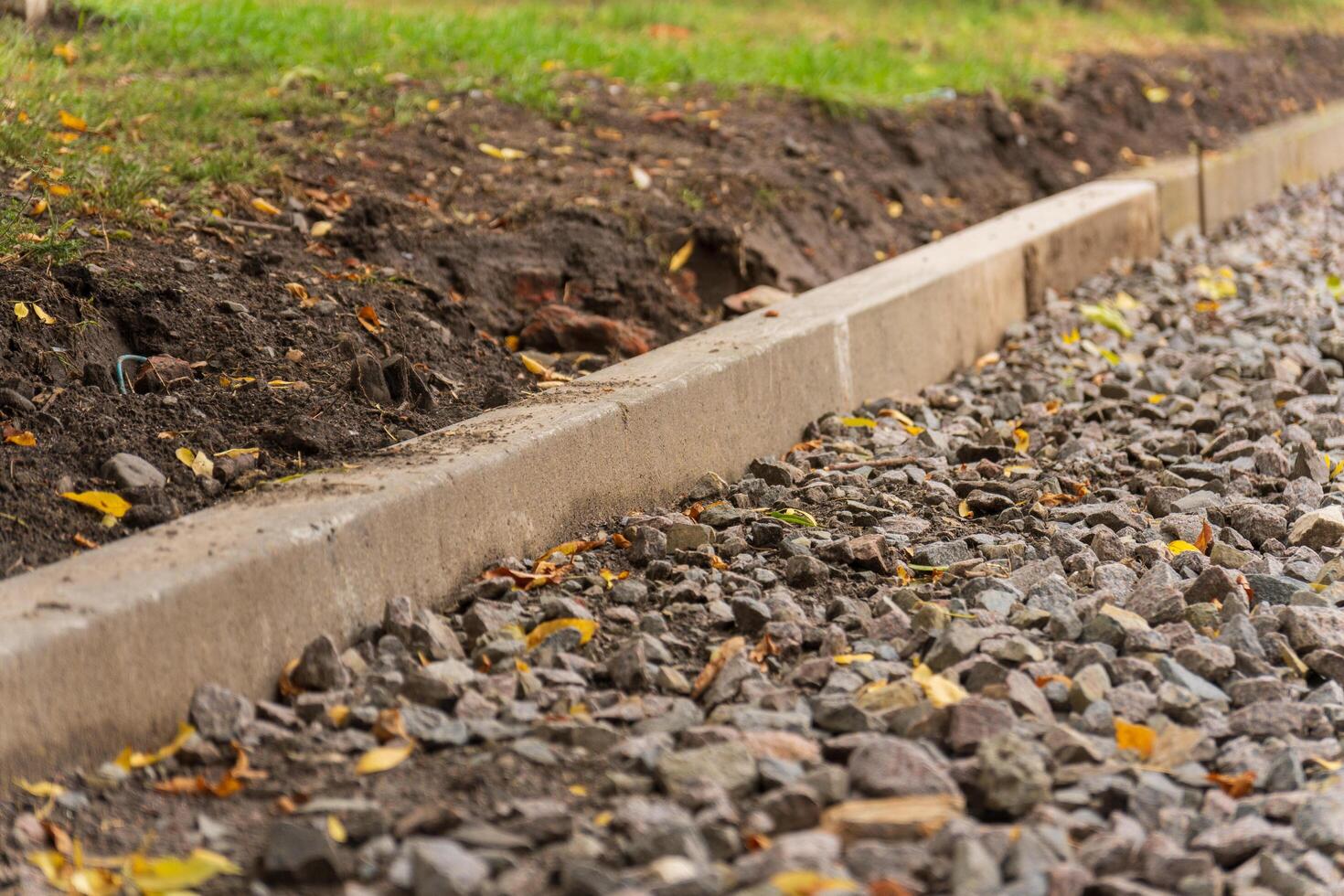 A concrete curb lines the edge of a gravel path. The path is covered in small, gray rocks. There is a grassy lawn to the left of the path photo