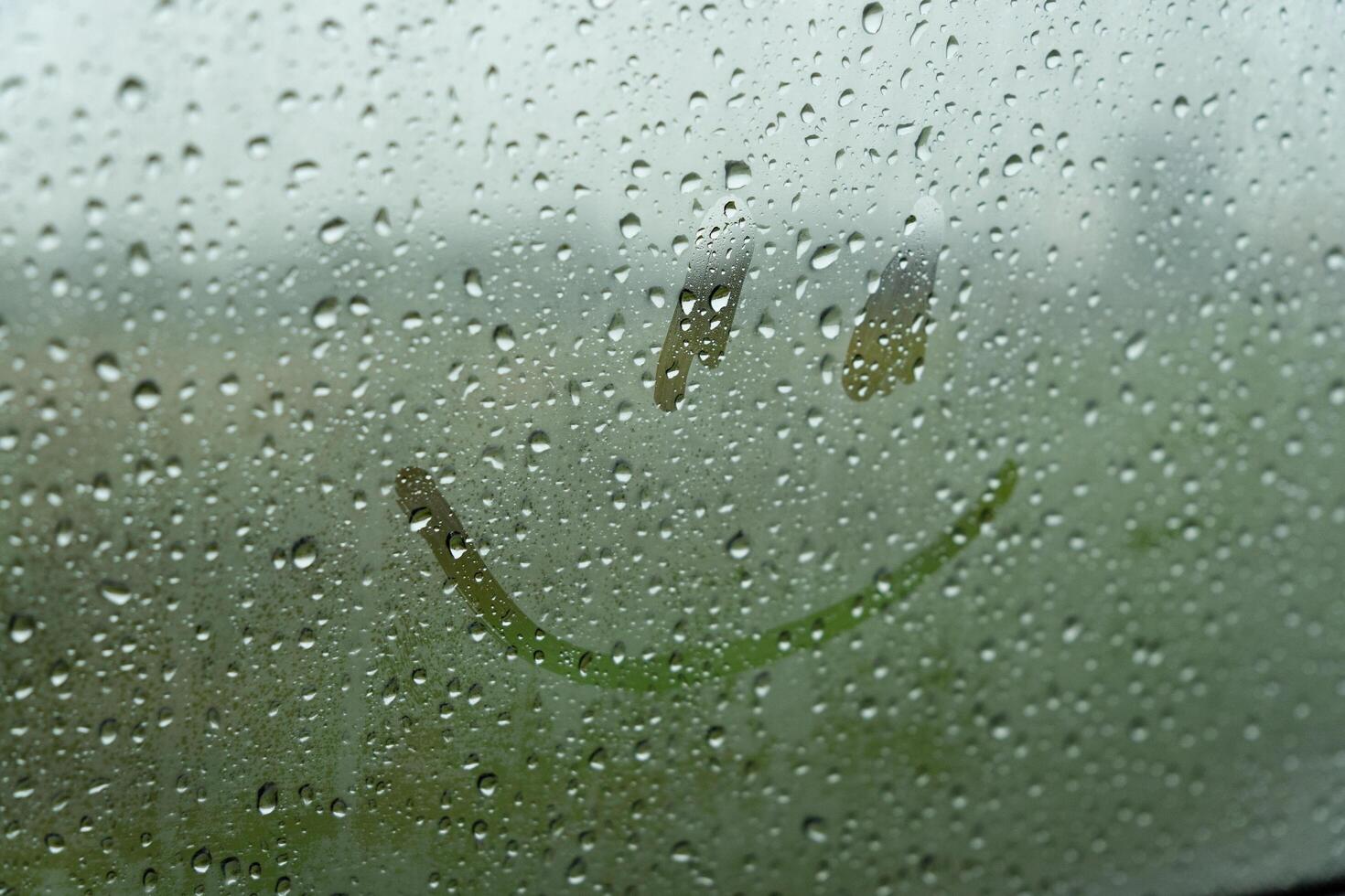 Raindrops create a dreamy backdrop as a playful smile emerges on the glass, mixing joy with the soothing sounds of a heavy downpour outside in nature photo