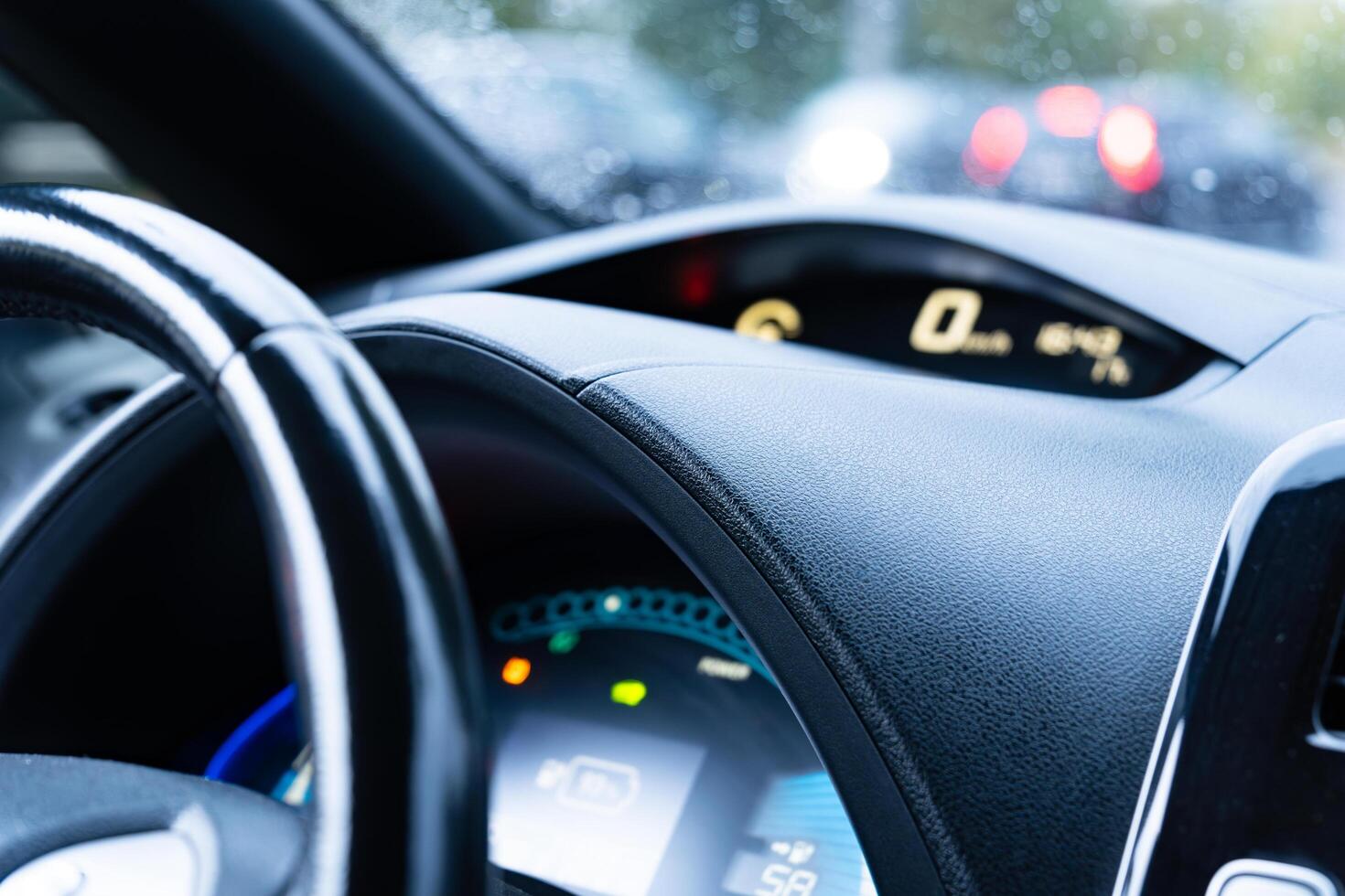 Raindrops on the windshield create a blurred backdrop while a driver's hand grips the steering wheel, focusing on the digital dashboard display photo