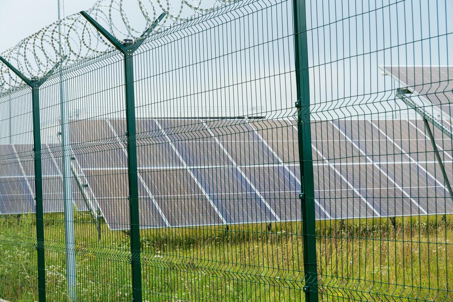 Rows of solar panels are installed within a secured area, featuring a green fence topped with barbed wire, showcasing a commitment to renewable energy photo