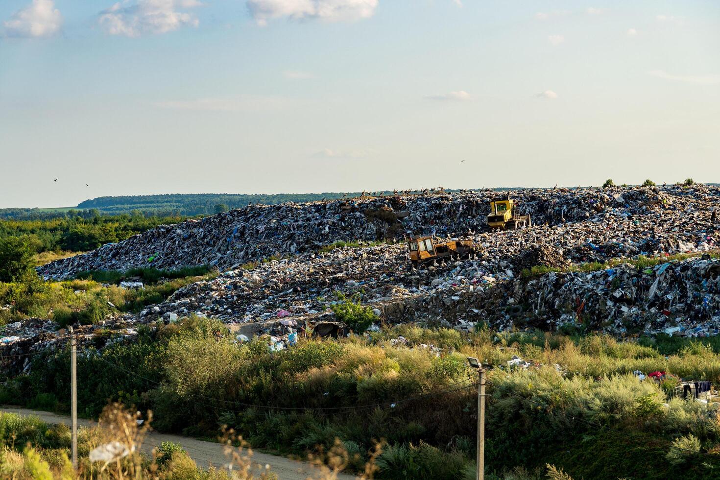 Mountains of refuse accumulate at a landfill site surrounded by greenery, highlighting the environmental impact of waste management practices under the afternoon sun photo