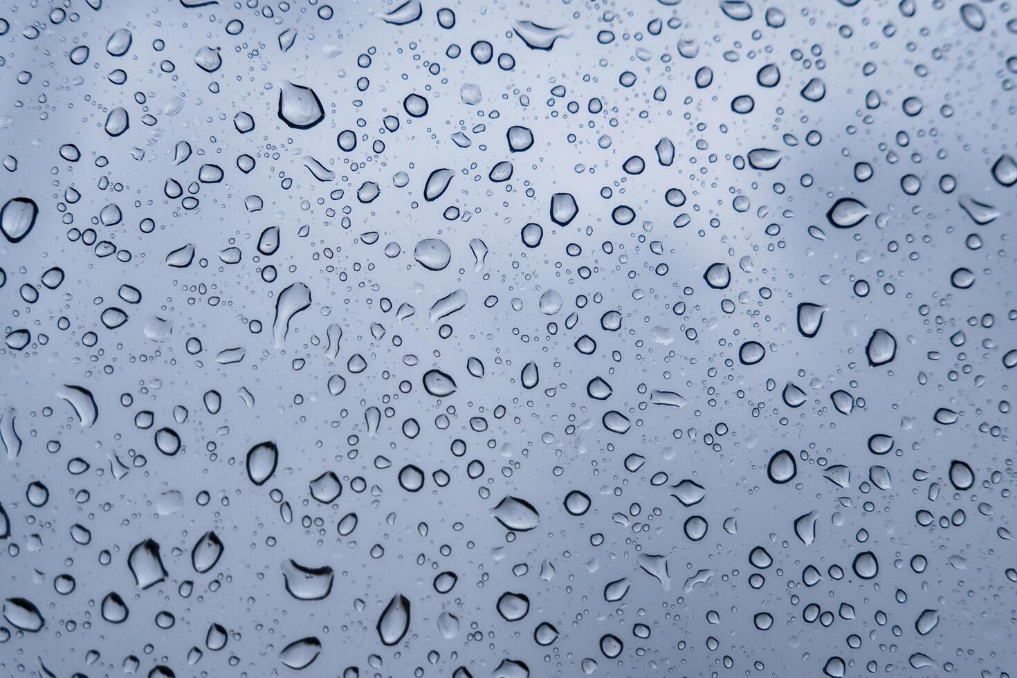 Delicate droplets accumulate on a window, blurring the view outside as gray clouds loom overhead during a quiet rainy afternoon photo