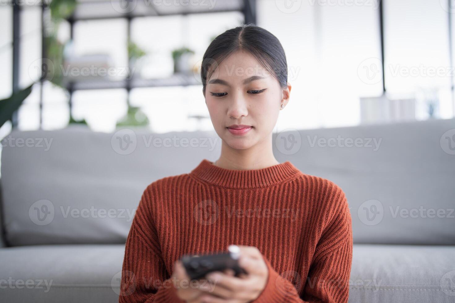Asian Woman controlling smart home. mobile phone with smart home app in living room. touch screen ai technology. Remote control system. photo