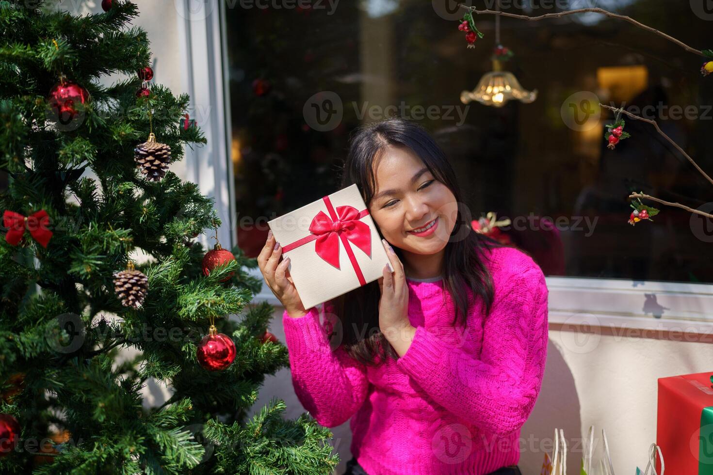 asian woman holding christmas gift box in front of christmas tree photo