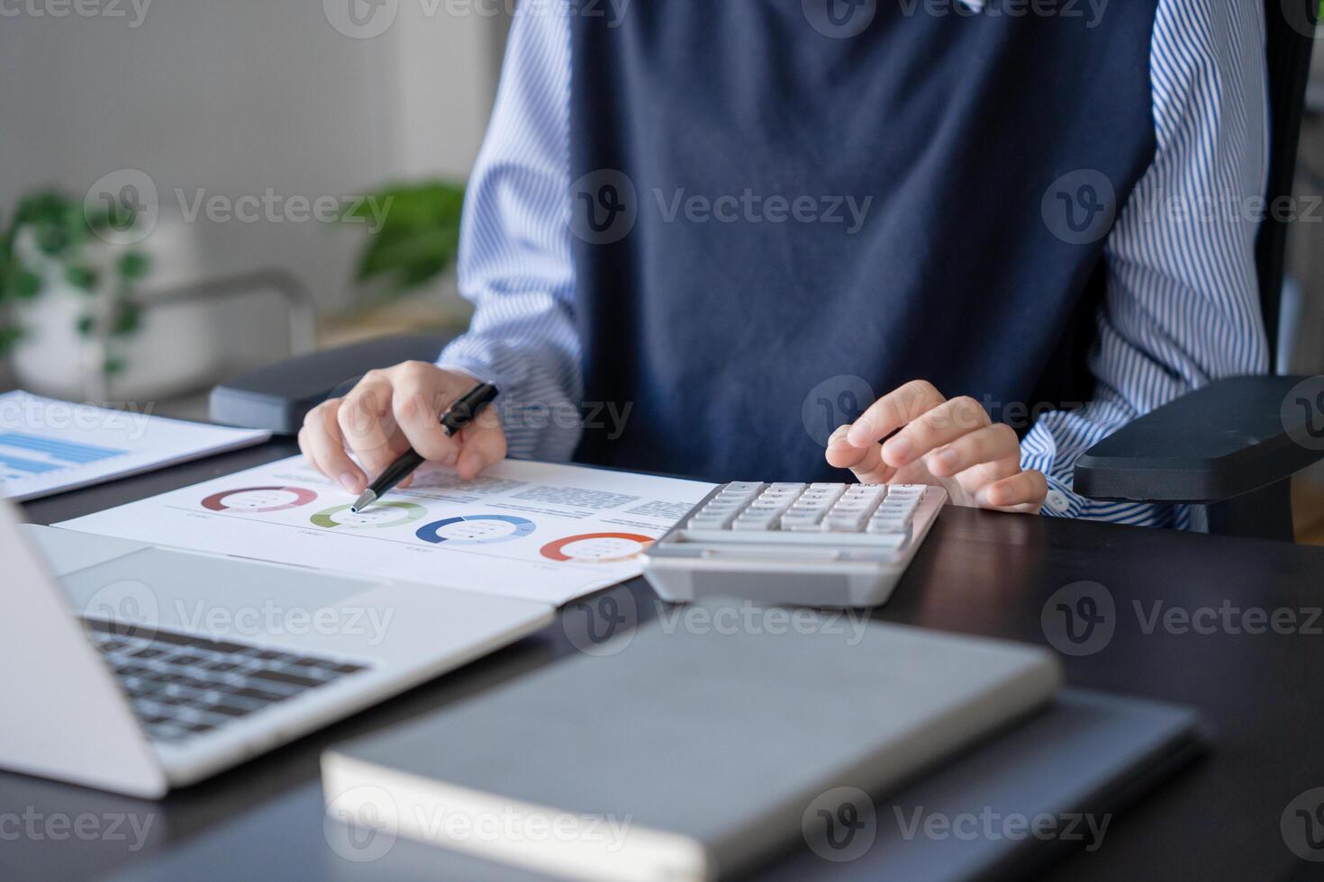 Asian businesswoman doing paper work with pen laptop calculator in room photo