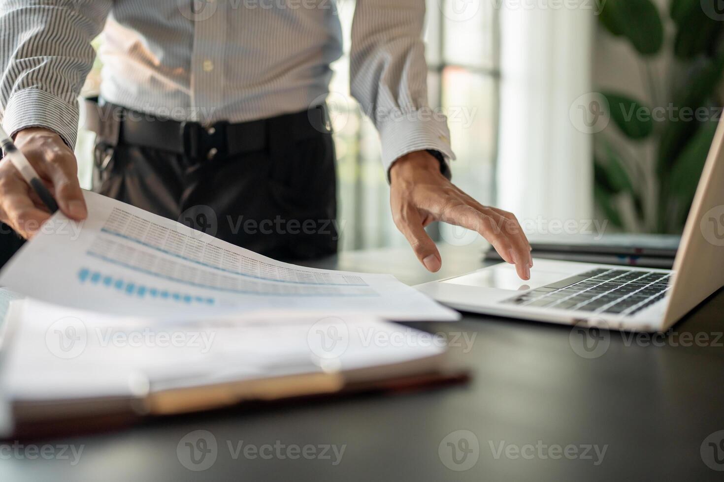 Accountant is holding a piece of paper while looking at a laptop photo