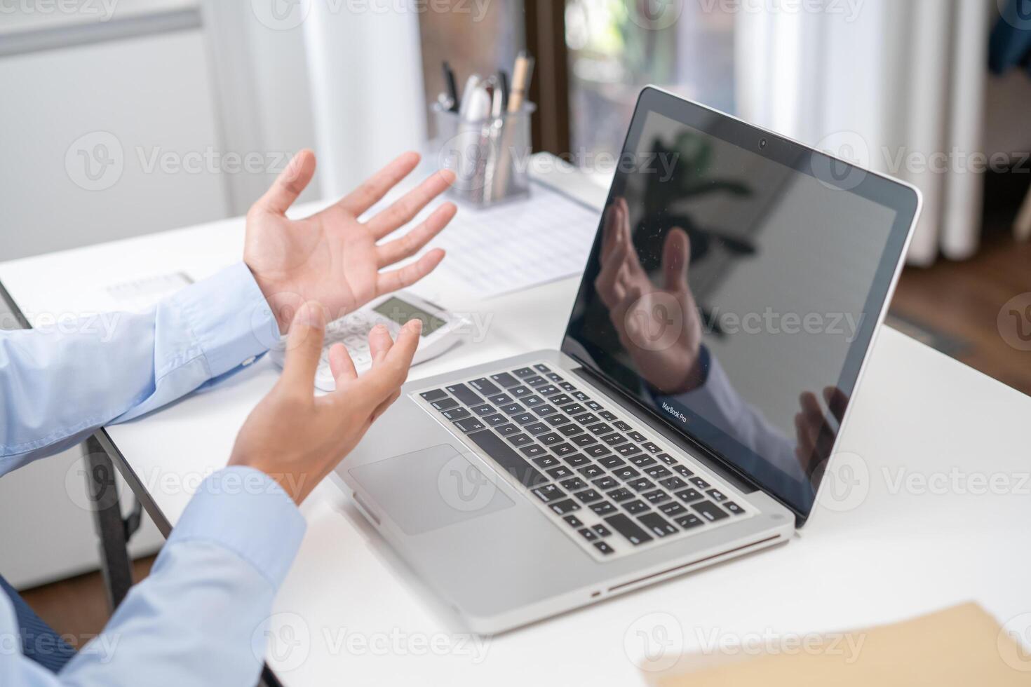 a man is gesturing while sitting at a desk with a laptop photo