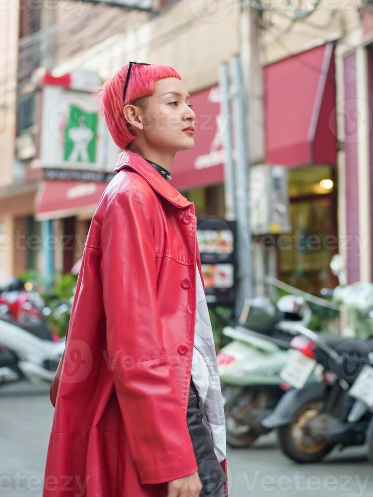 a gen z woman with pink hair and a red coat is walking down the street photo