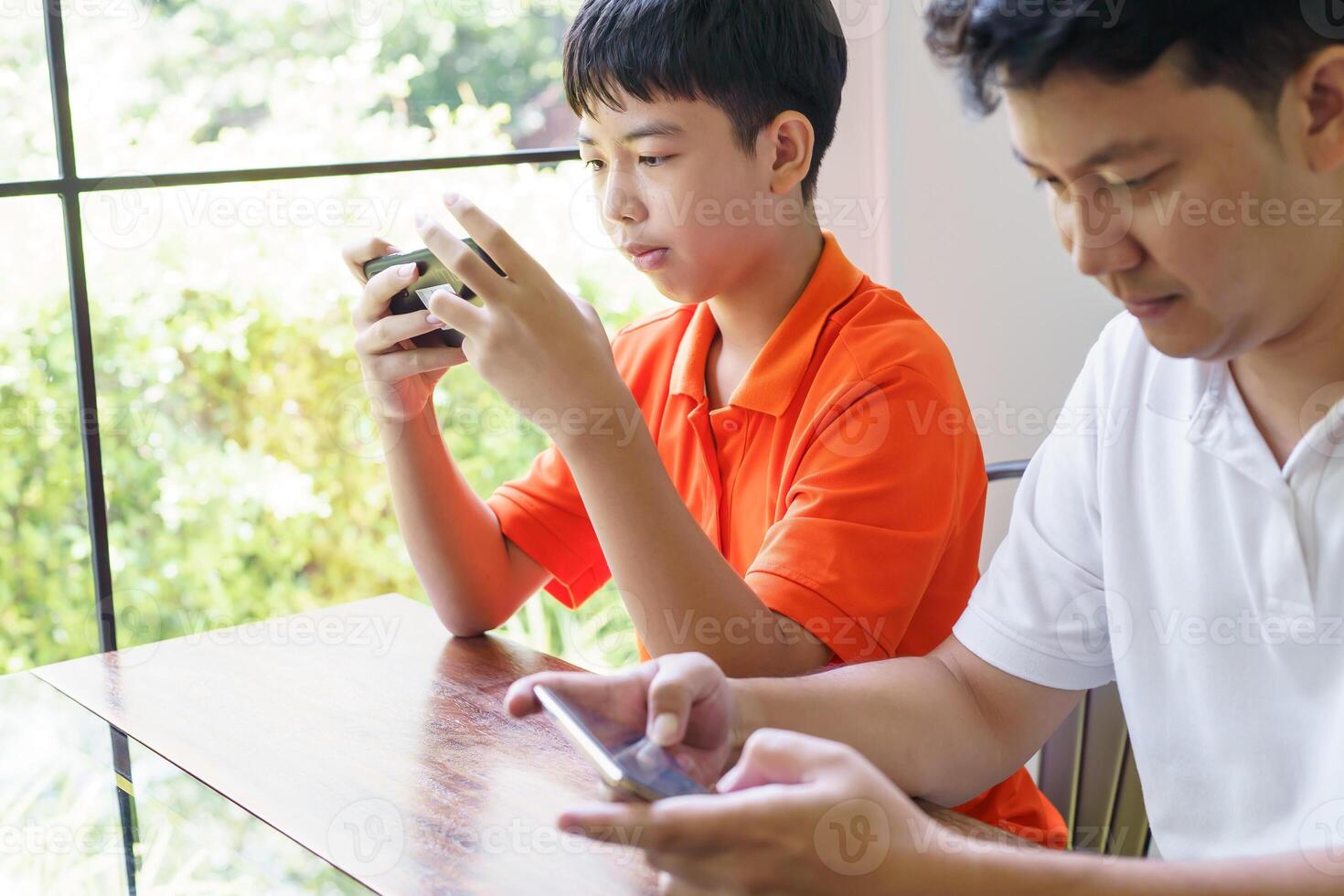 a man and a boy sitting at a table looking at their cell phones photo