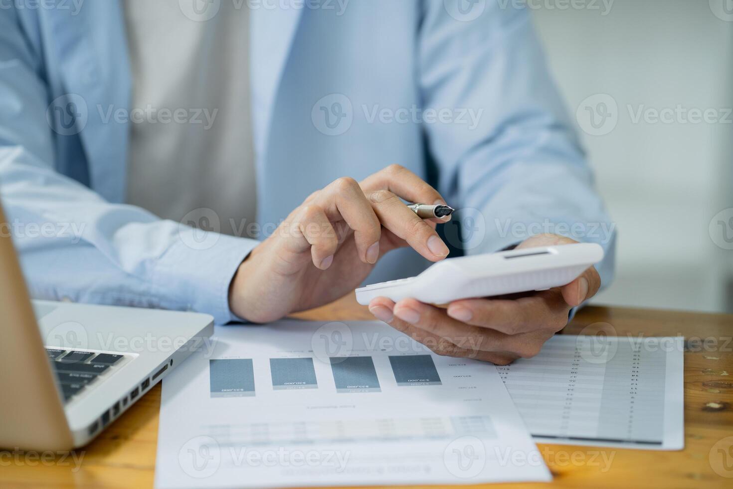 a man is using his calculator while sitting at a desk with a laptop and papers photo
