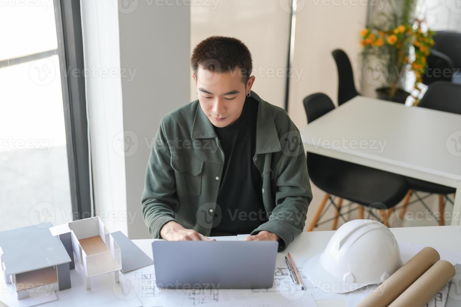 Architecture man sitting at a table with a laptop and construction paper photo