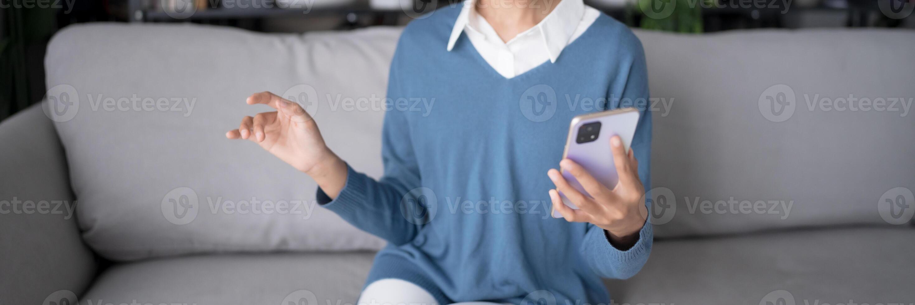 a woman sitting on a couch holding a cell phone using voice assistant photo