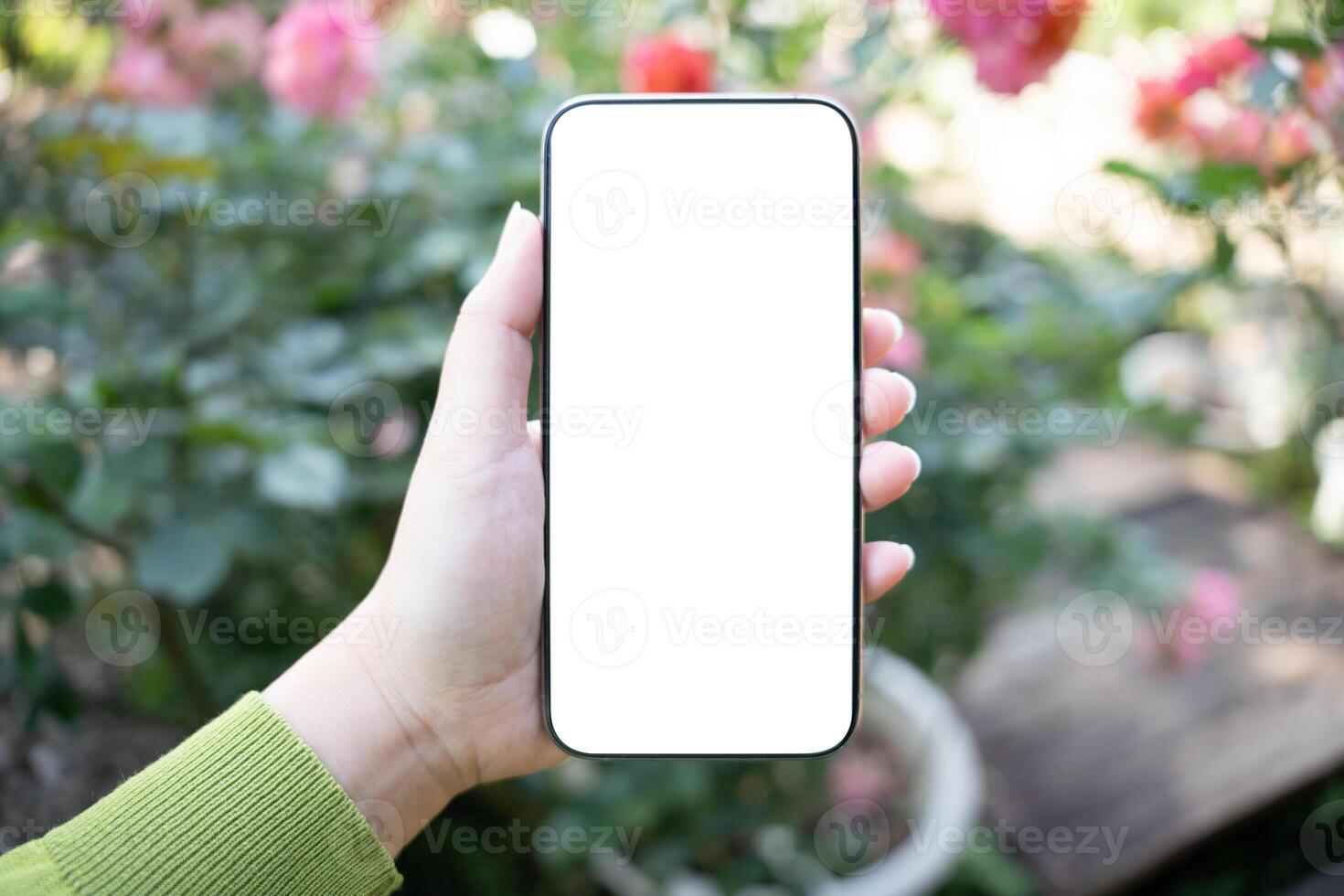 a person holding up a blank white phone screen in front of a garden photo