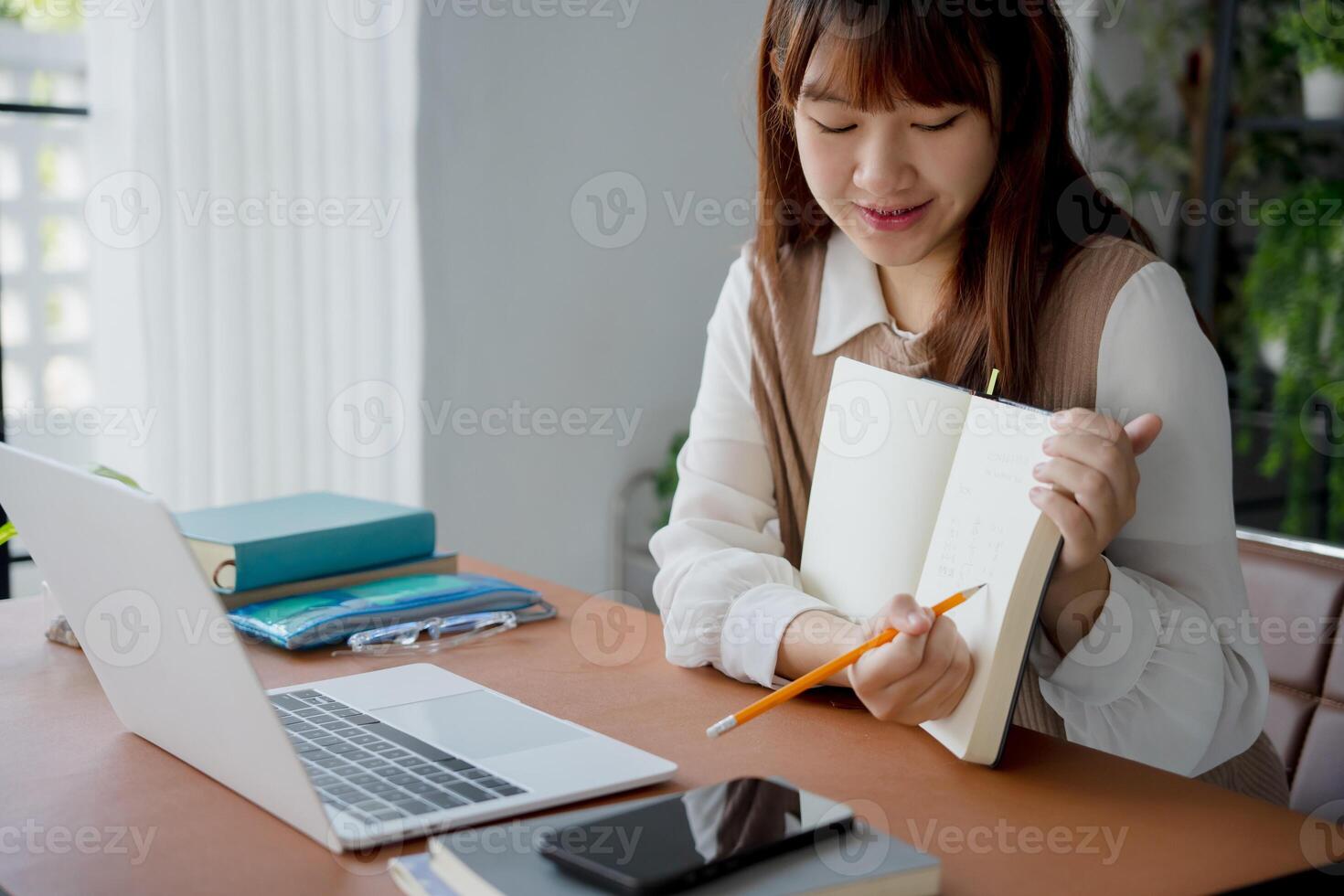 a student woman is sitting at a table with a notebook and a laptop photo