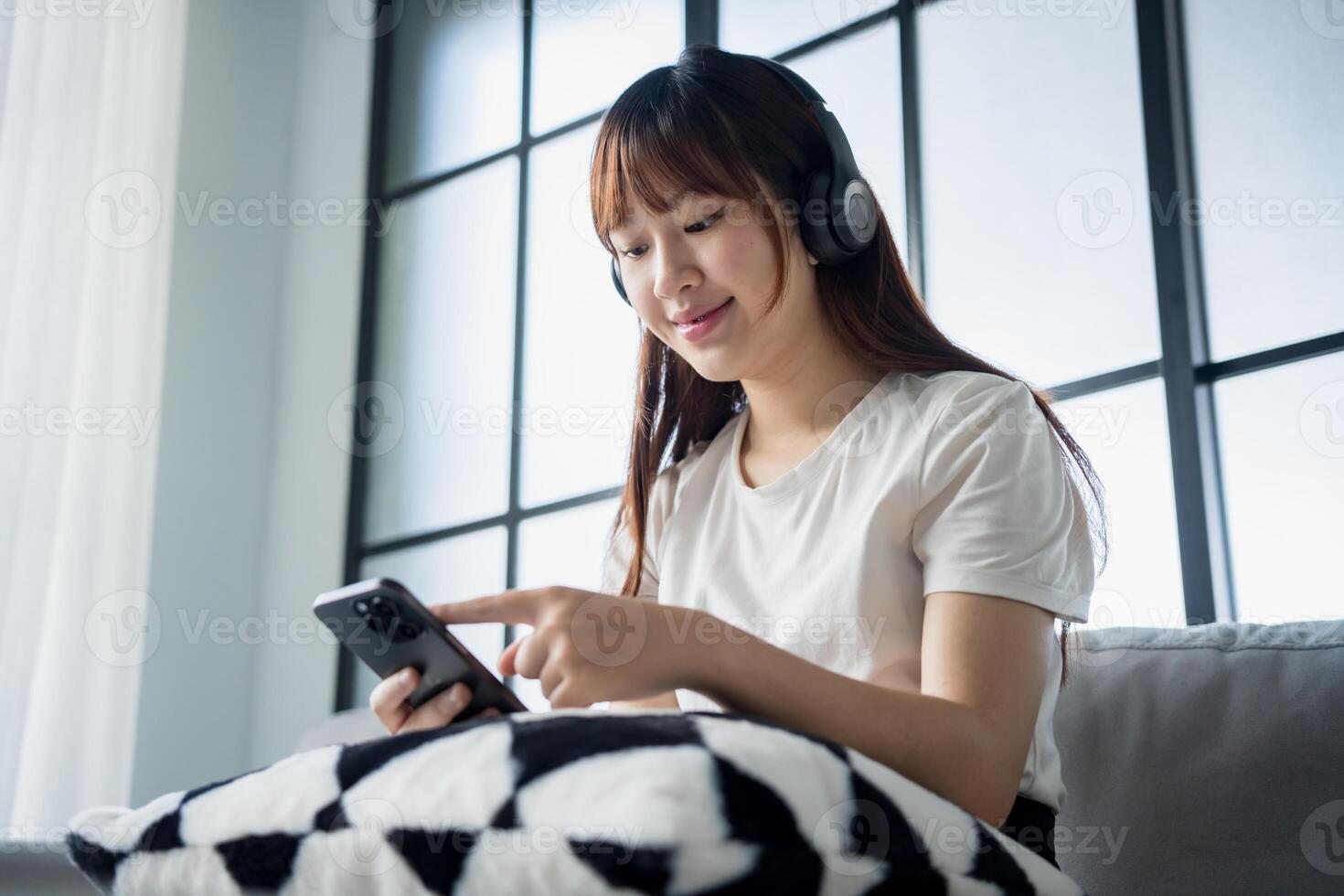 asian woman using smartphone while sitting on couch in living room. photo