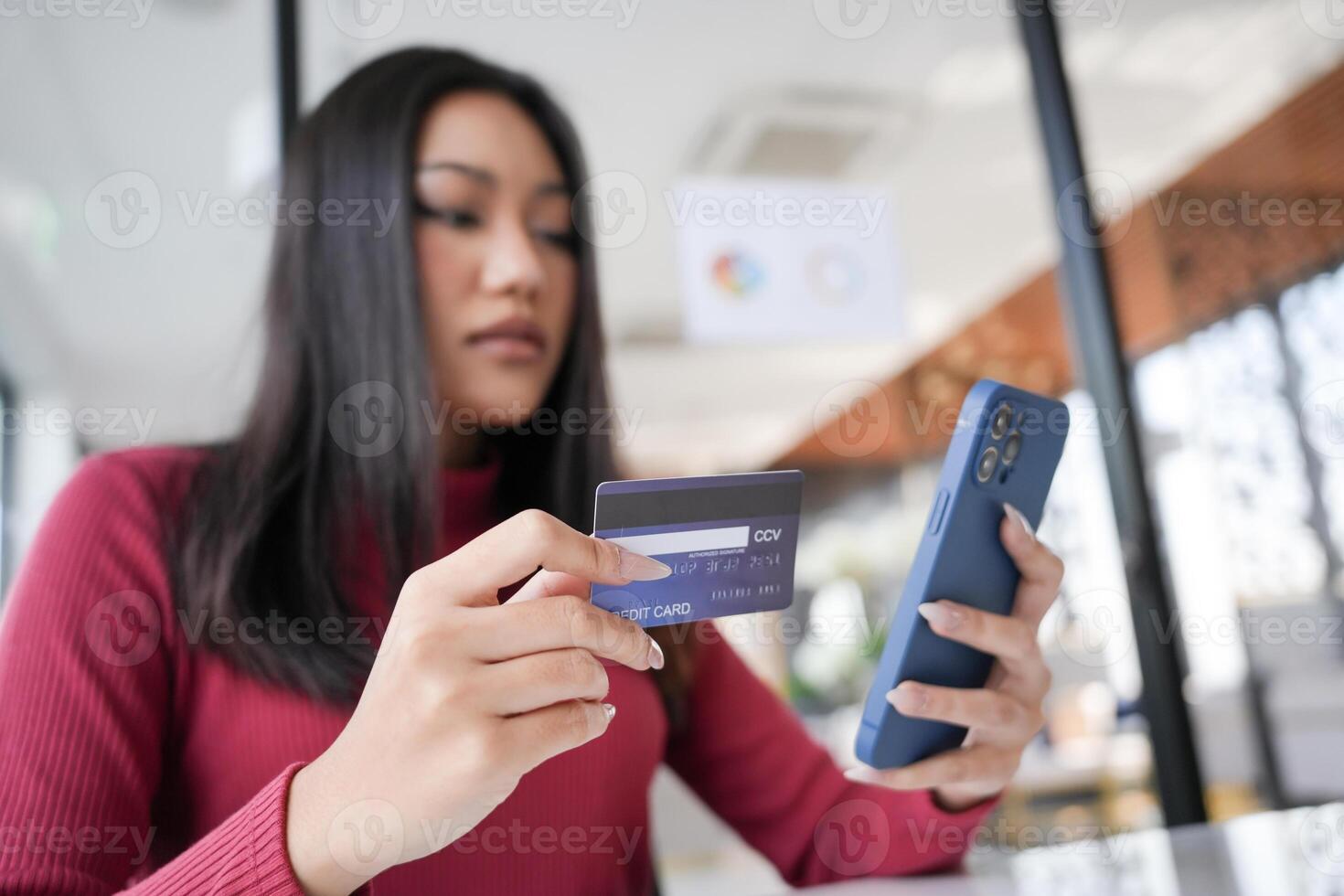 a woman holding a credit card and looking at her phone. photo