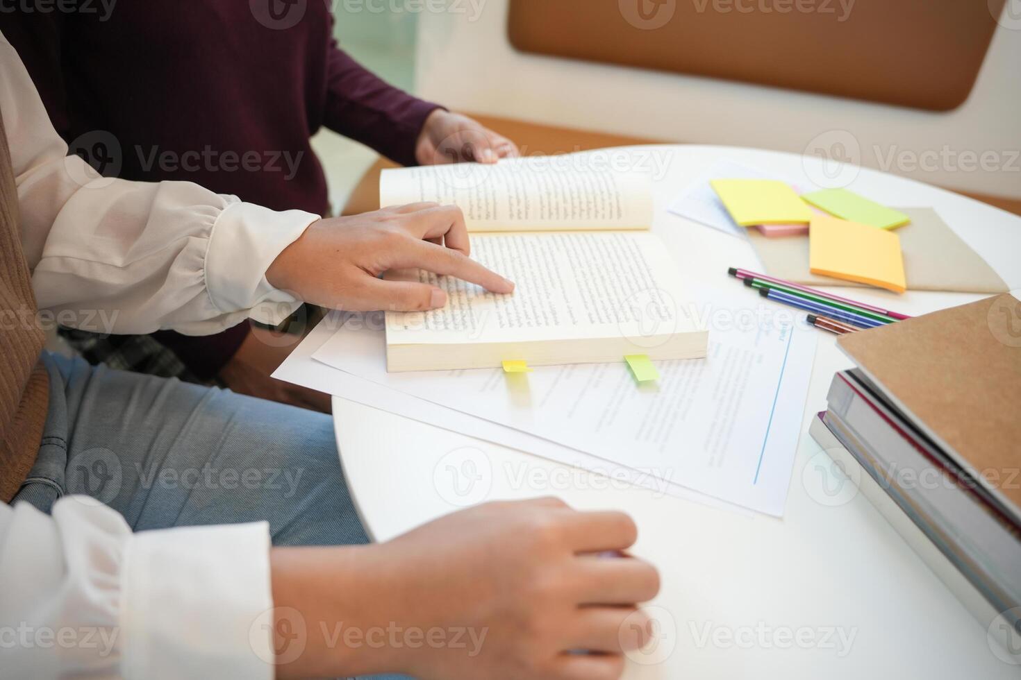 two people sitting at a table with books and pens learning together photo