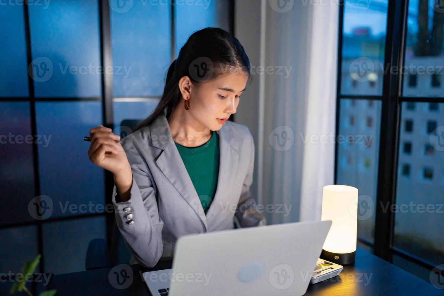 Alone Working Late at Night, a woman in a business suit sitting at a desk with a laptop photo