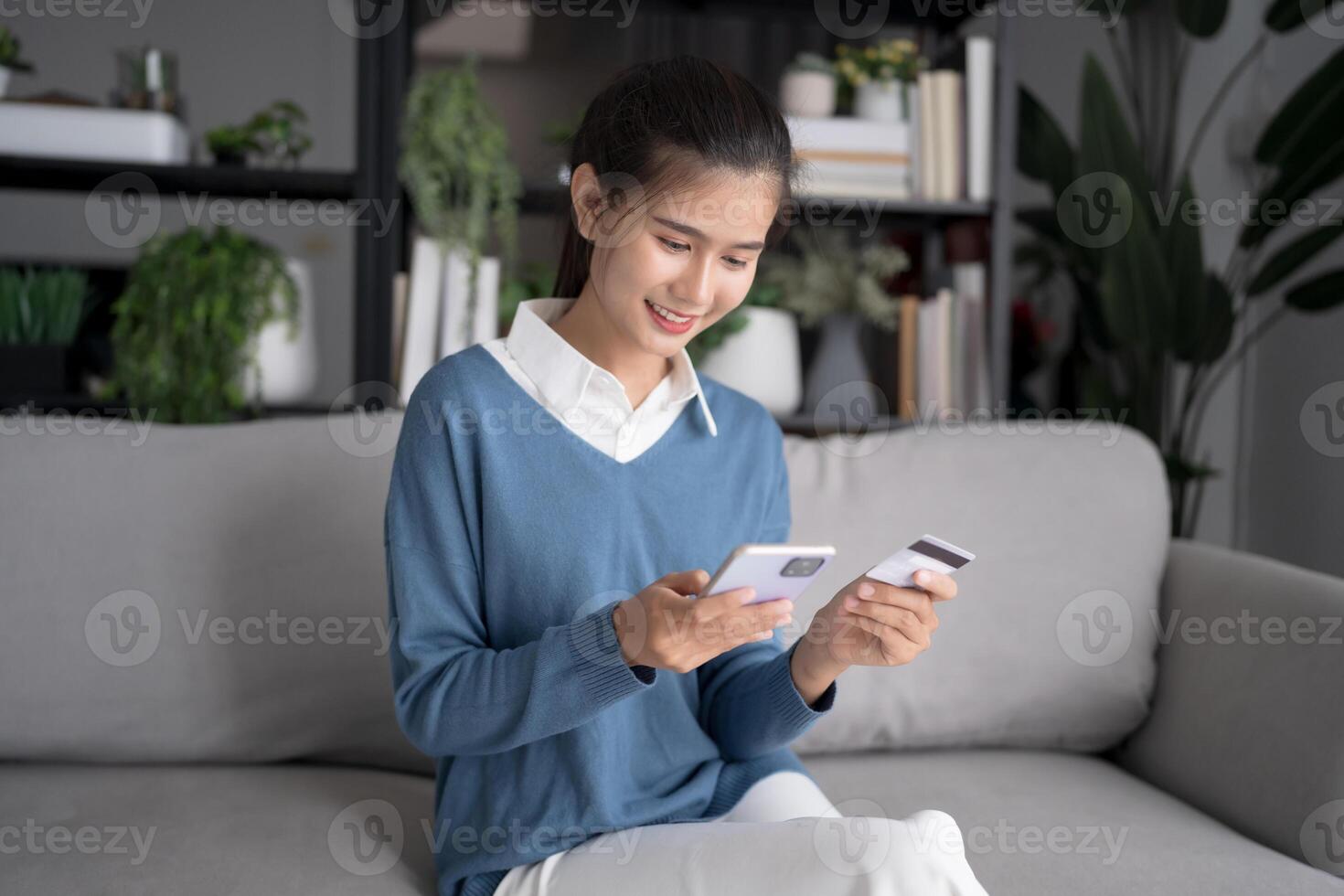 a woman sitting on a couch holding a credit card and smartphone photo