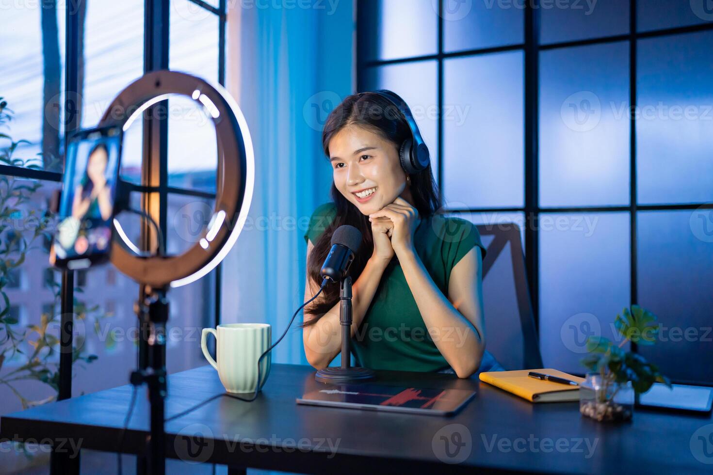 Content creator woman in a green shirt is sitting at a desk with a microphone and a camera photo