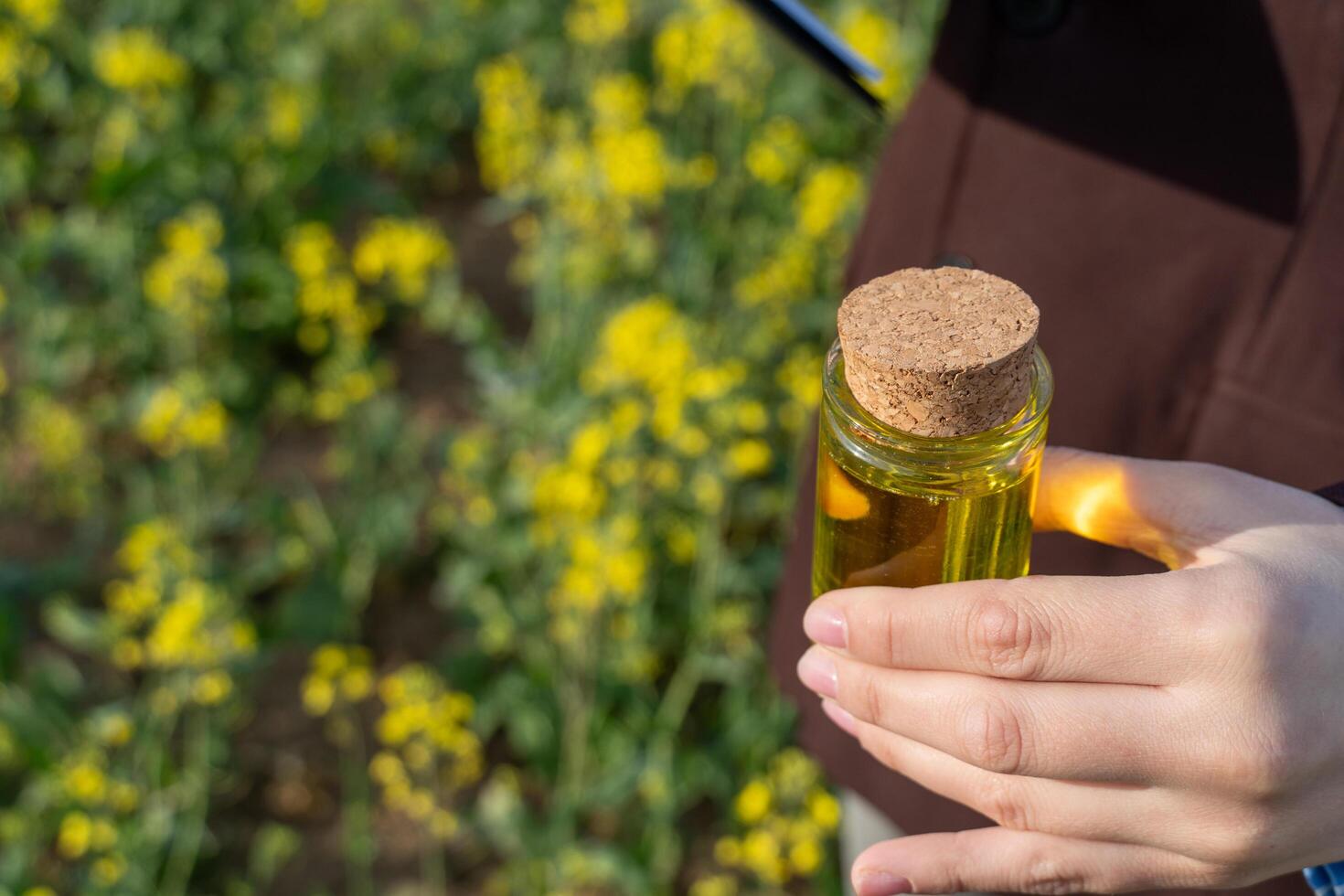 Woman holding a glass jar containing yellow liquid with a cork, with a field of flowers in the background. photo
