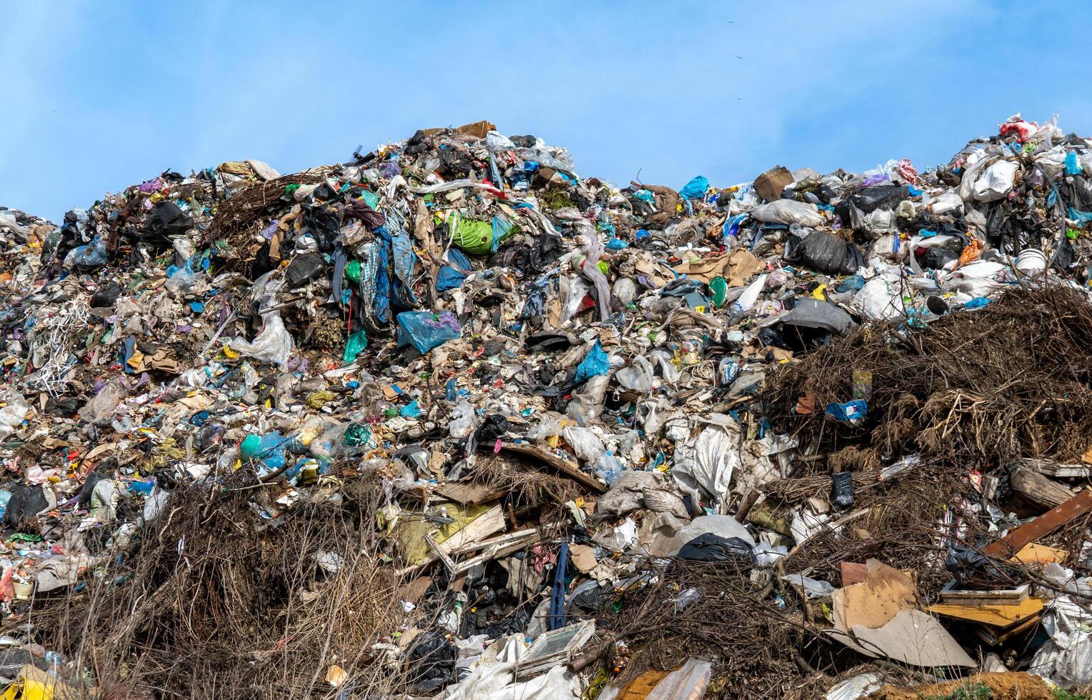 Overfilled refuse hill shows environmental damage with garbage, refuse, trash and plastic bags under bright blue sky. photo