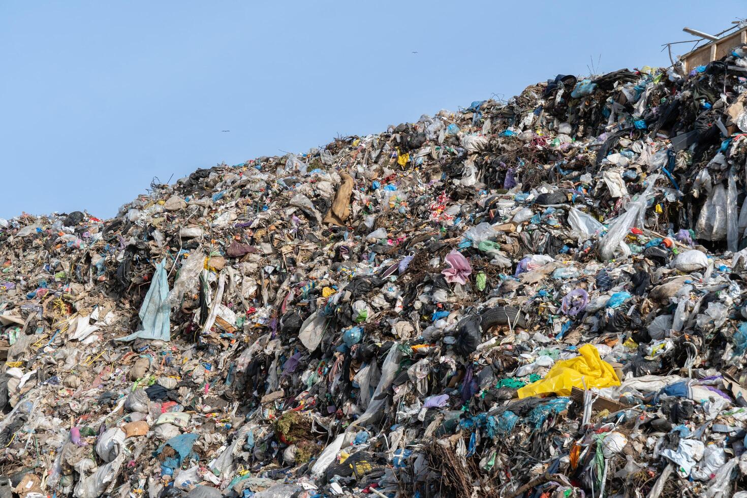 Overflowing landfill under sunny sky, showcasing waste accumulation, pollution problems, and environmental concerns on large refuse heap photo