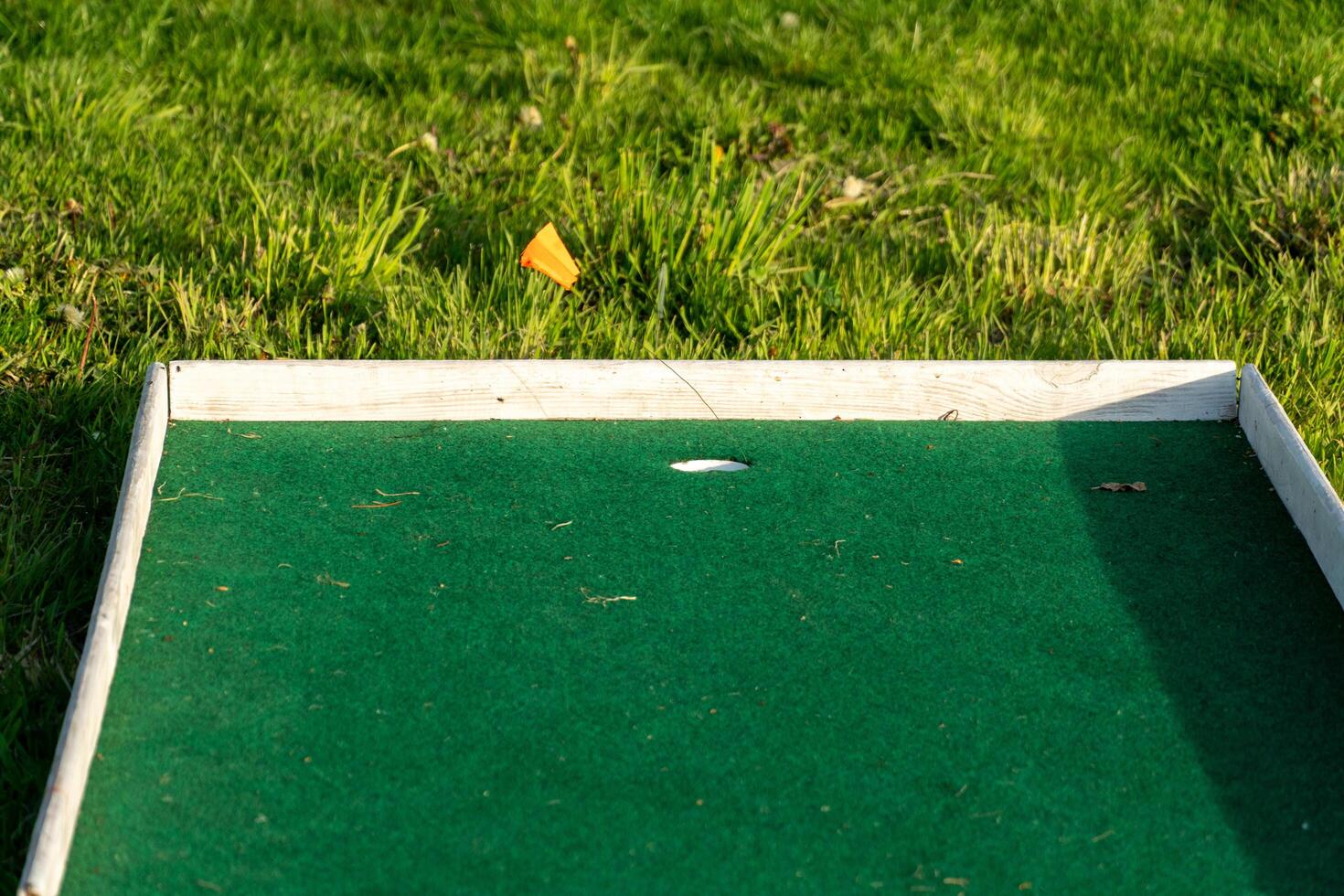 Close-up of a Miniature Golf Course Hole with Green Turf and Grass, Featuring a Small Orange Flag for Direction photo