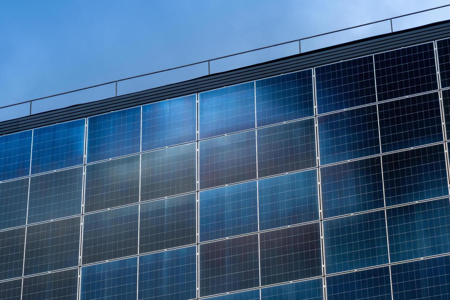 Exterior shot of large solar panel array on building facade against clear blue sky, reflecting daylight and providing renewable energy photo