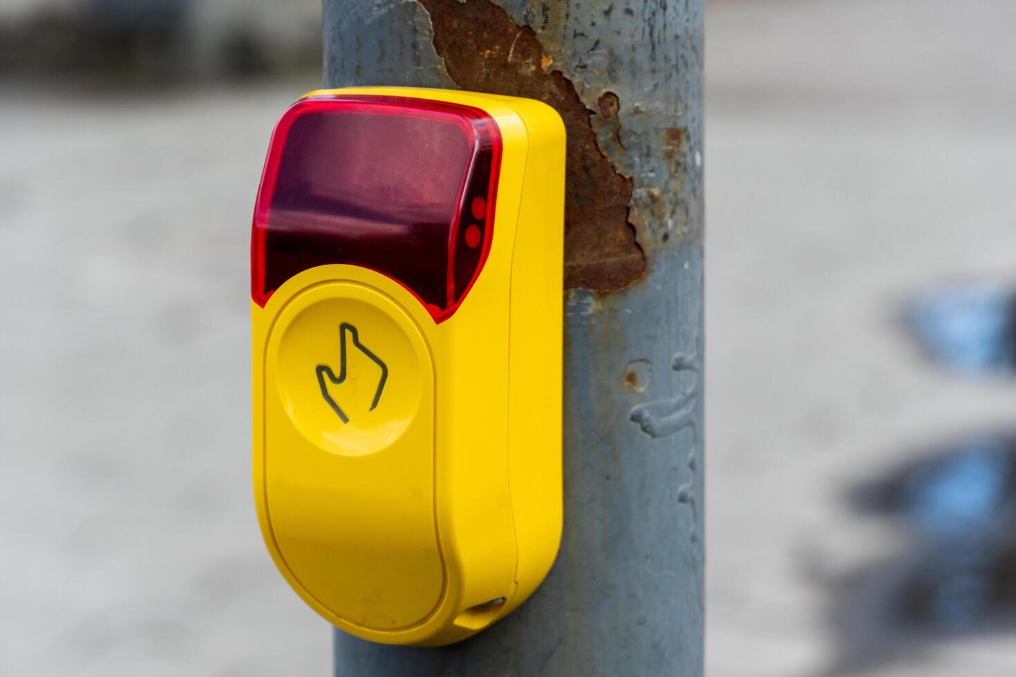 Pedestrian crosswalk signal button with hand symbol on weathered metal pole, yellow box with red light signaling safe crossing photo