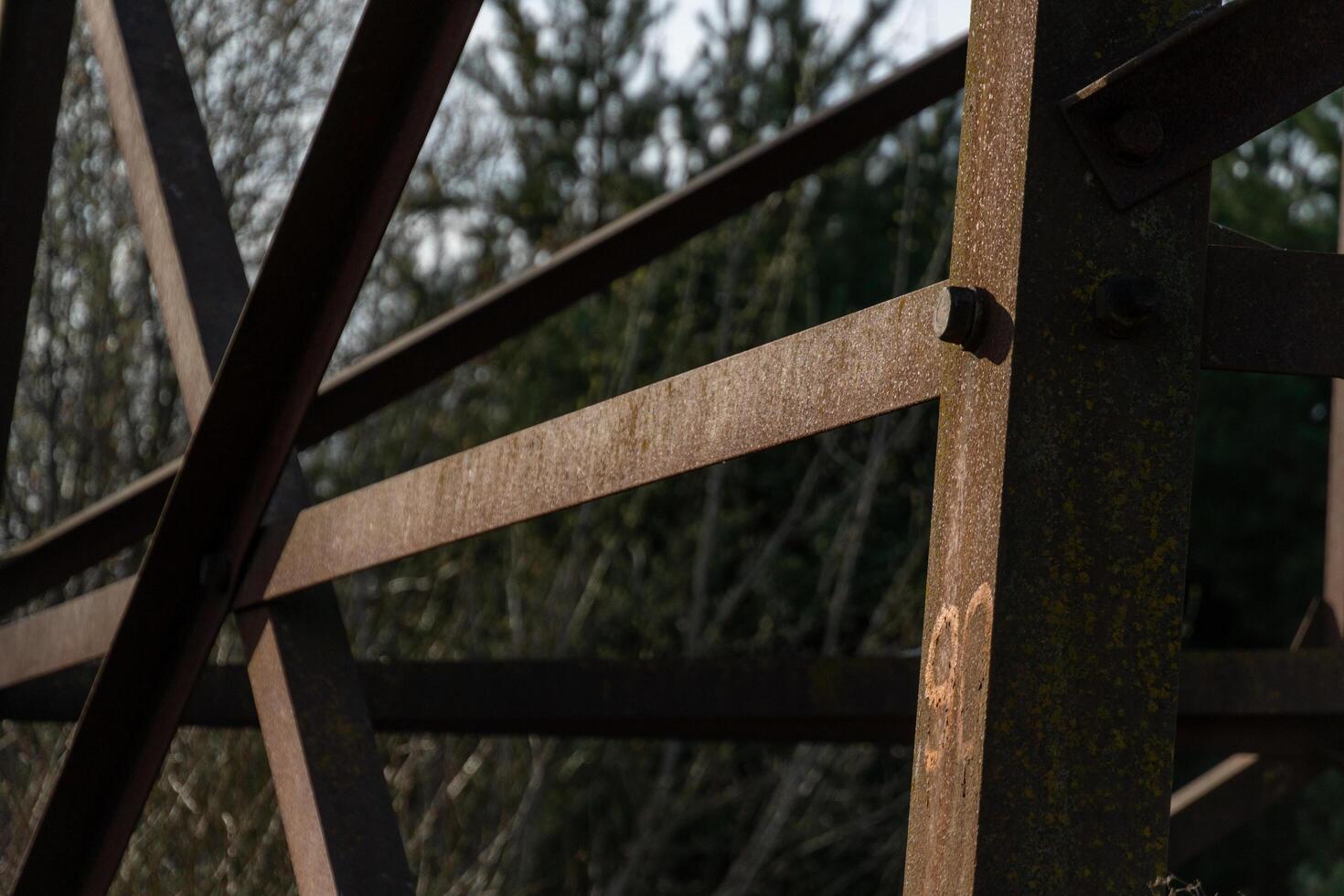 Old weathered rusty metal structure with bolted joints set against an unfocused outdoor woodland backdrop on a sunny day photo