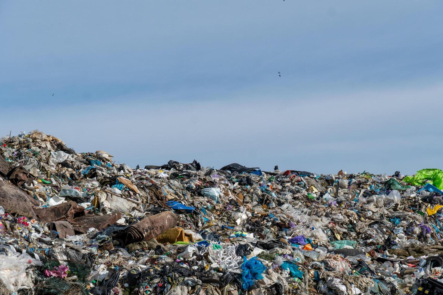 Massive Waste Pile under Sky Reveals Consumption and Environmental Concerns, Featuring Various Discarded Items photo